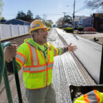 Construction contractor wearing gear and working on stripping road with tool and riding on back of truck