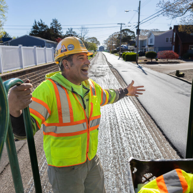 Construction contractor wearing gear and working on stripping road with tool and riding on back of truck
