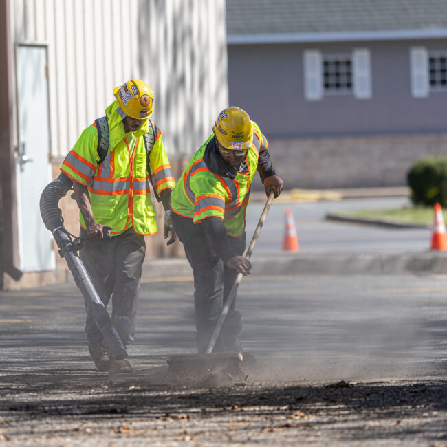 Construction workers stripping asphalt back from commercial parking lot