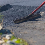 Rake pushing asphalt cement on road near drain