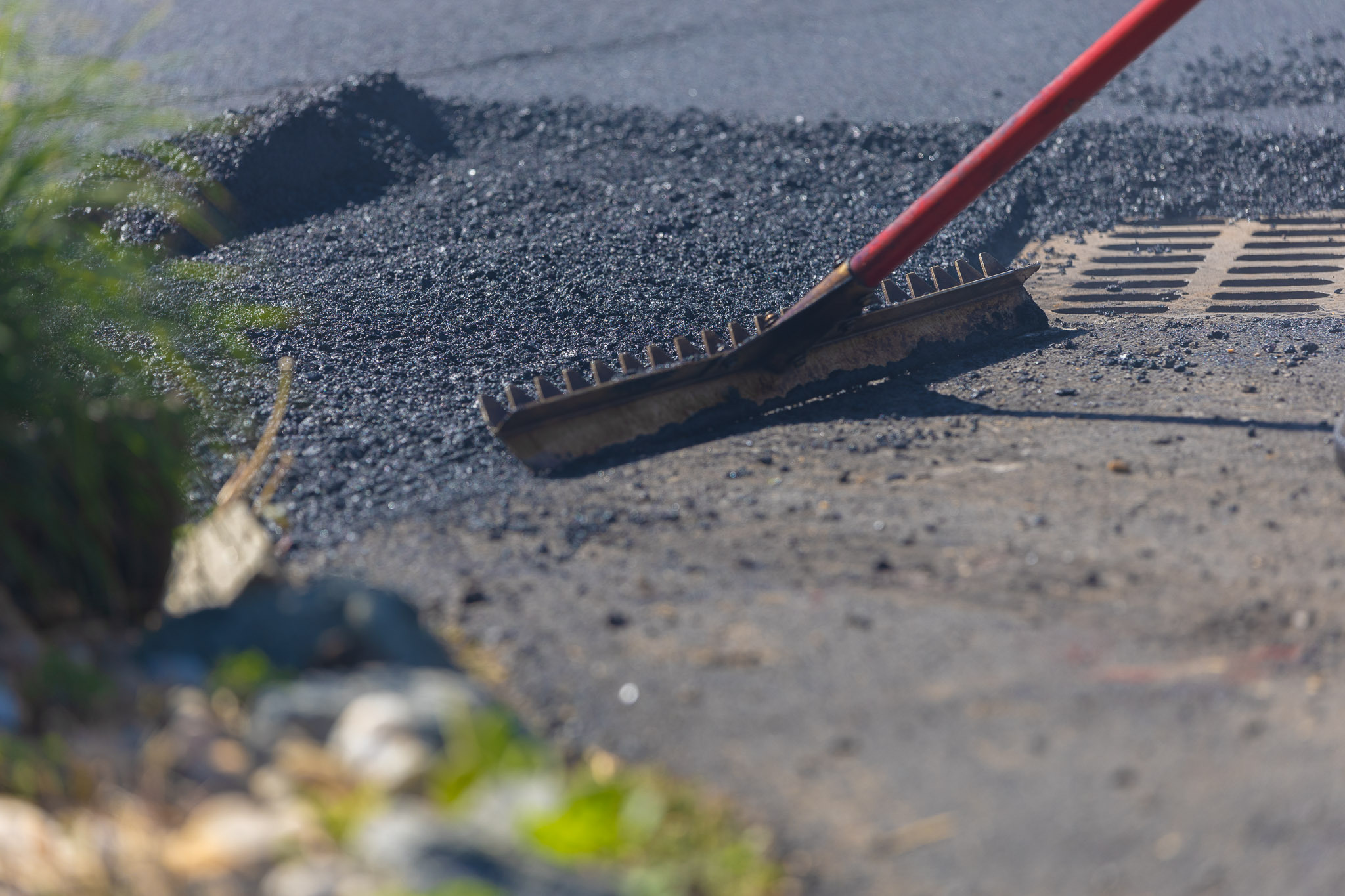 Rake pushing asphalt cement on road near drain