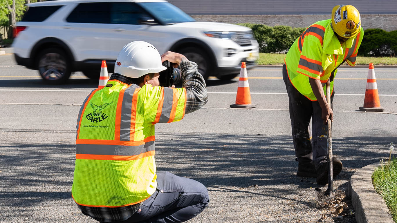 Two construction workers excavating road and surveying with traffic cones and SUV in background
