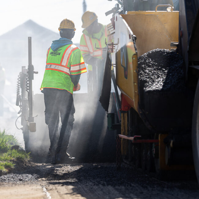 Workers mixing and pouring asphalt from truck and spreader