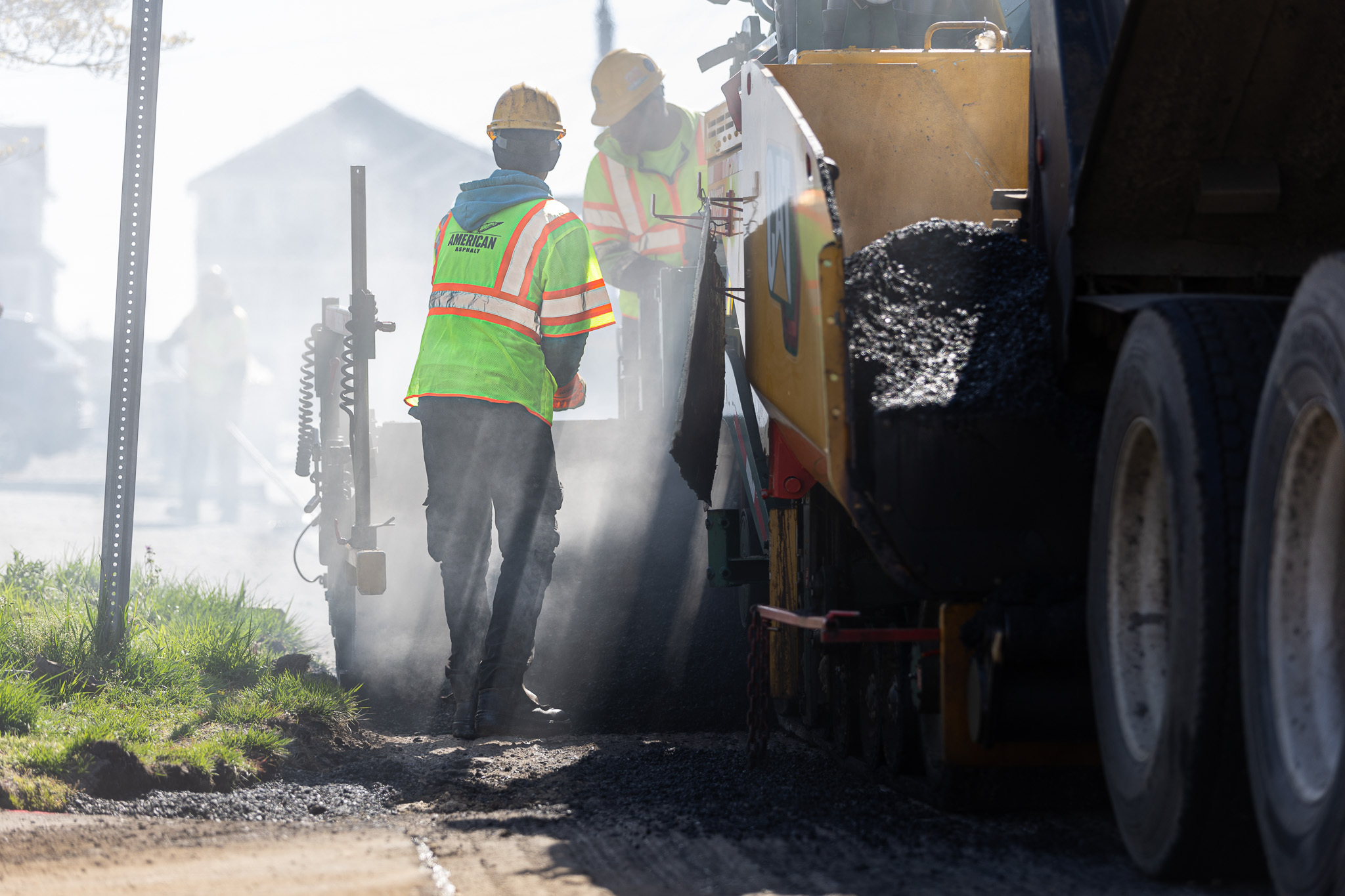 Workers mixing and pouring asphalt from truck and spreader
