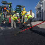 Construction crew working on spreading asphalt across new home parking lot with truck spreader behind them