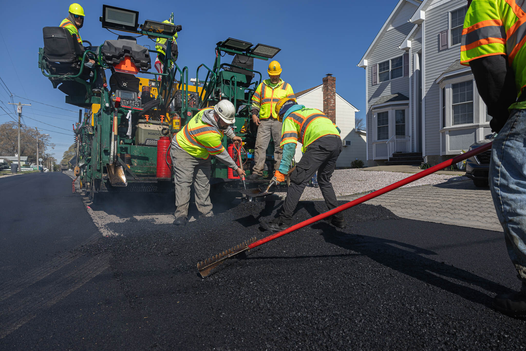 Construction crew working on spreading asphalt across new home parking lot with truck spreader behind them