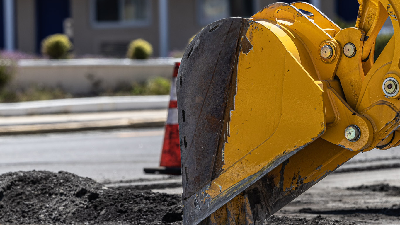 Construction machinery digging up asphalt outside apartment building